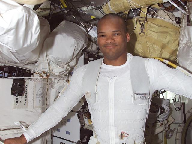Astronaut Robert Curbeam inside, wearing a white bodysuit and smiling at the camera.