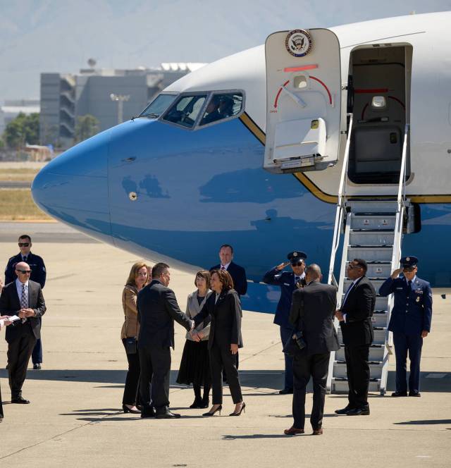 A man and a woman shake hands in front of a small group of people standing outside a plane with stairs descending from its open door.