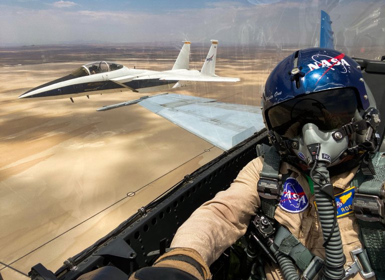 Selfie over the shoulder of a person flying in an airplane. Out of the side window over the shoulder of the person is a second airplane in flight.