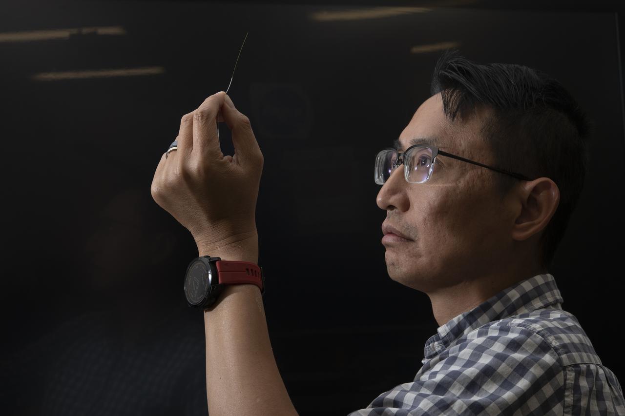 A picture of Patrick Chan, electronics engineer, and NASA Armstrongs FOSS portfolio project manager, closely examining an optic fiber inside of a protective sleeve.