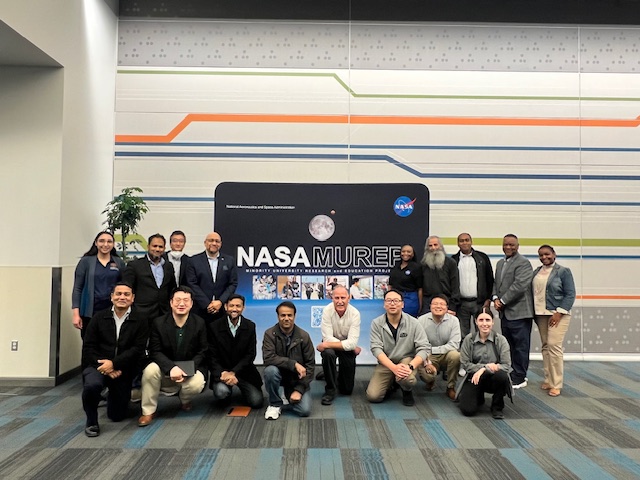 A group of people standing and kneeling around a pop-up banner with NASA MUREP and an image of the Moon