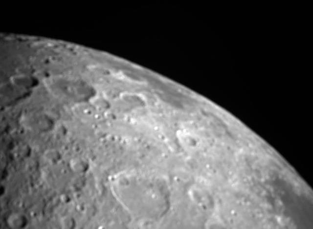 An image of the Moon that curves through the middle of the image, with the cratered lunar surface in the lower left half of the image and the black of space in the upper right half.