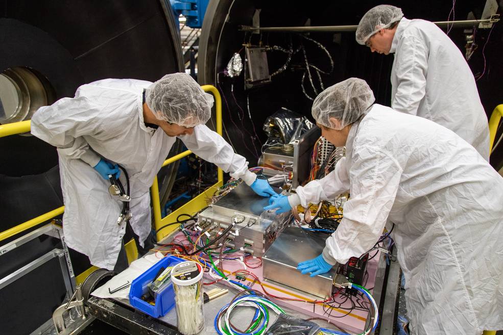 This photograph shows three people standing on either side of NASAs ComPair balloon instrument before it goes into a thermal vacuum chamber for testing.
