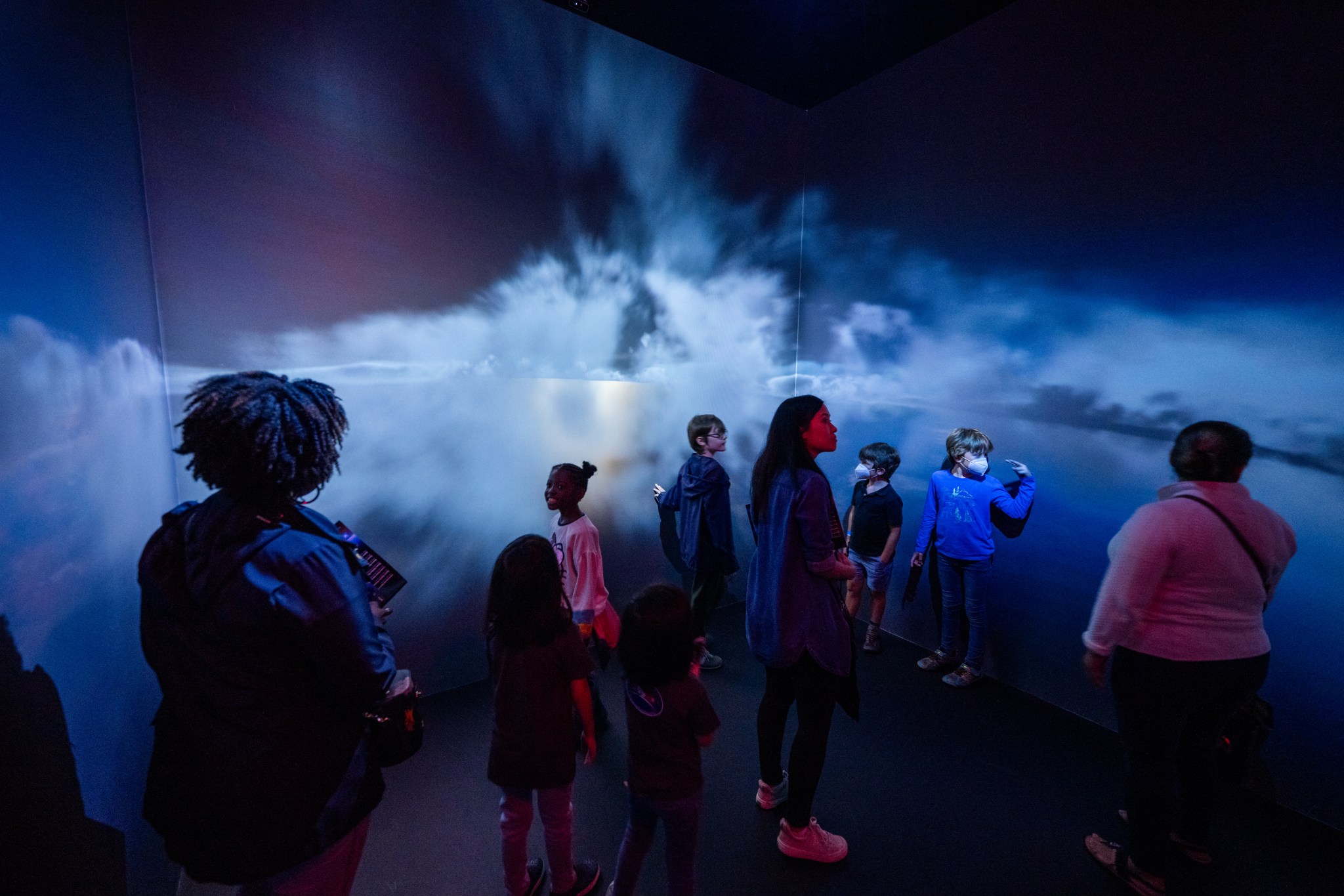 Students walking through an immersive multimedia experience with the Earth below them and they are engulfed in clouds.
