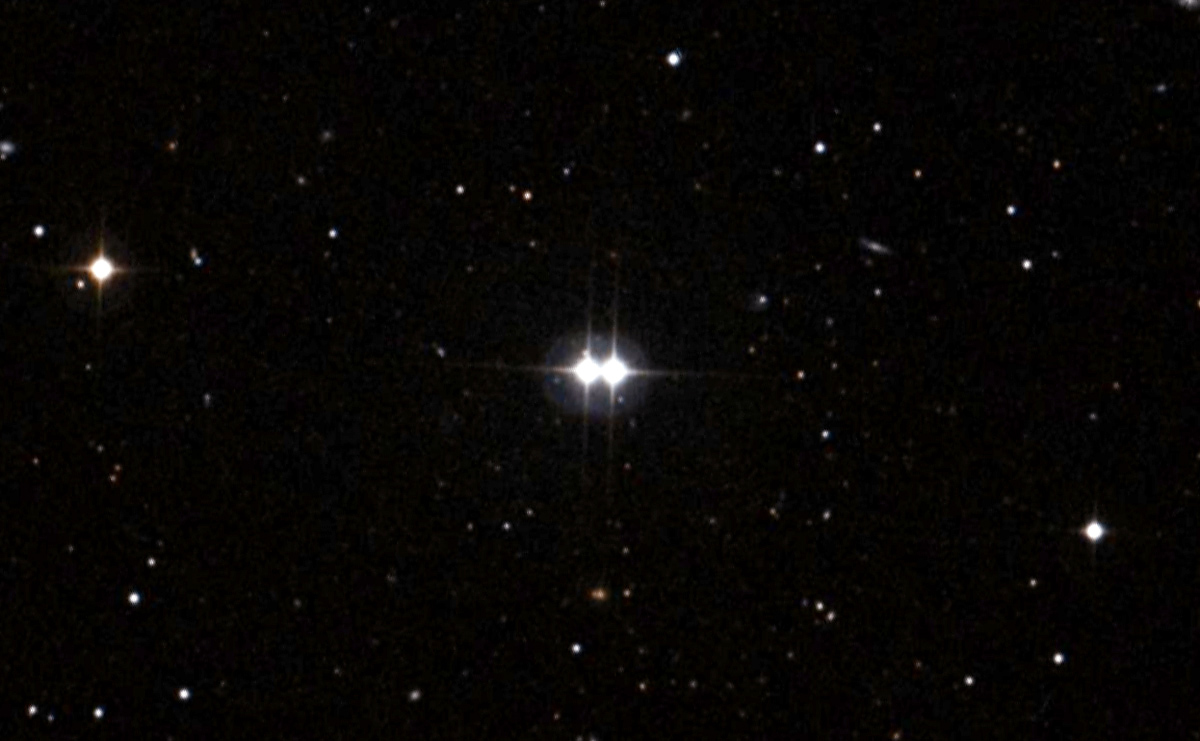 A pair of bright, close stars with diffraction spikes shine at the center of a field of faint stars against the blackness of space.