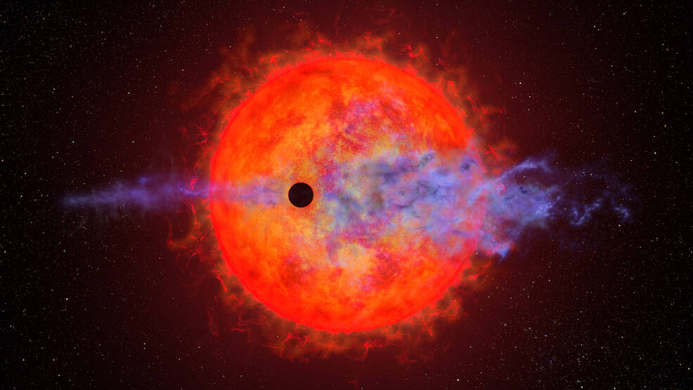 Illustration: mottled red dwarf star with finger-like outbursts. Foreground: small black circle, a planet passing in front of the star. Star is stripping planet's atmosphere, appearing as wispy-blue filaments along the planets orbital path.