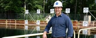 A man stands in a white hardhat with the NASA logo on it in front of water
