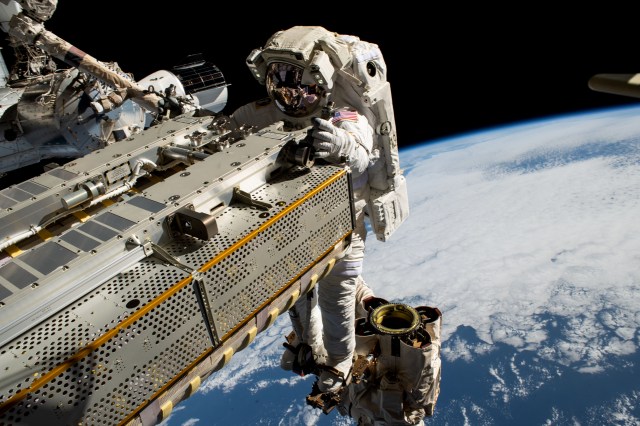 Astronaut Woody Hoburg rides the Canadarm2 robotic arm while maneuvering a roll-out solar array during a spacewalk.