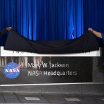 Bryan Jackson, grandson of Mary W. Jackson, left, and Raymond Lewis, son-in-law of Mary W. Jackson, right, unveil the Mary W. Jackson NASA Headquarters sign during a ceremony officially naming the building, Friday, Feb. 26, 2021, at NASA Headquarters in Washington, DC.