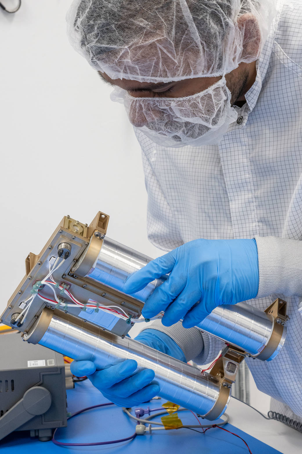 A person with blue gloves, a lab suit, and mask is holding a device. The device has two cylinders connected together.
