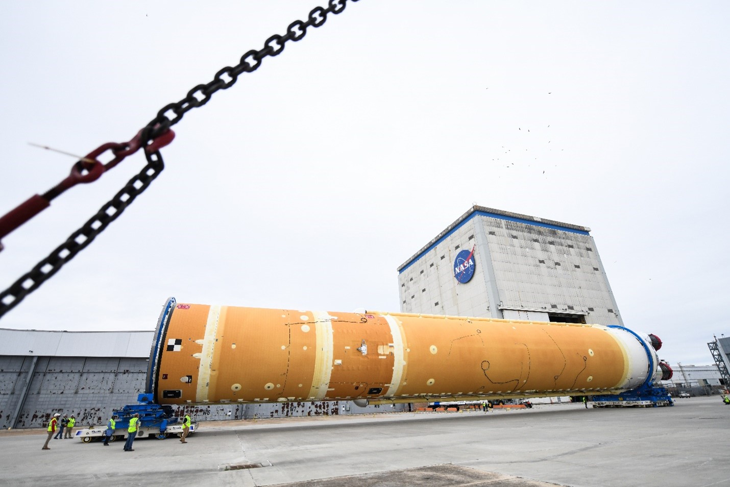 The large orange core stage of the SLS rocket is on it's side in front of Michoud Assembly Factory as it gets moved in 2020.
