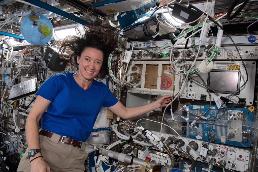 Astronaut Megan McArthur aboard the International Space Station smiles while pointing to an experiment developed by the Girl Scouts of the USA.