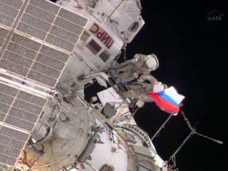 Near the end of their 5-hour, 58 minute spacewalk, Flight Engineers Fyodor Yurchikhin and Alexander Misurkin unfurl a Russian flag in commemoration of Russian Flag Day.