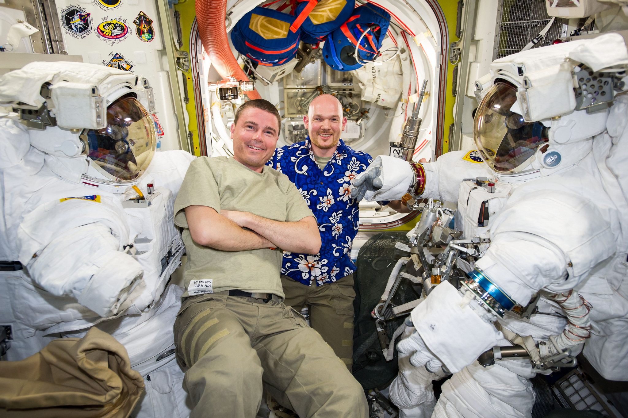 Astronauts Reid Wiseman and Alexander Gerst work with two spacesuits in the Quest airlock of the International Space Station while preparing for two spacewalks.
