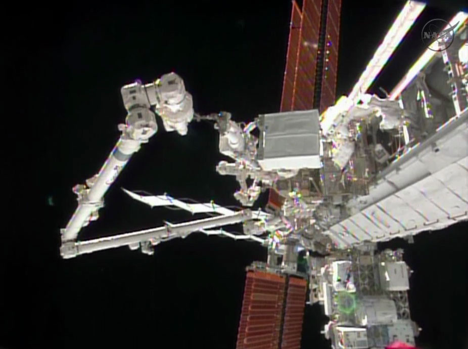 Spacewalker Mike Hopkins rides the Canadarm2 robotic arm carrying the ammonia pump module to the Starboard 1 truss worksite.