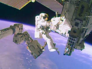 Astronaut Mike Hopkins prepares to attach himself to a foot restraint on the Canadarm2 outside the International Space Station.
