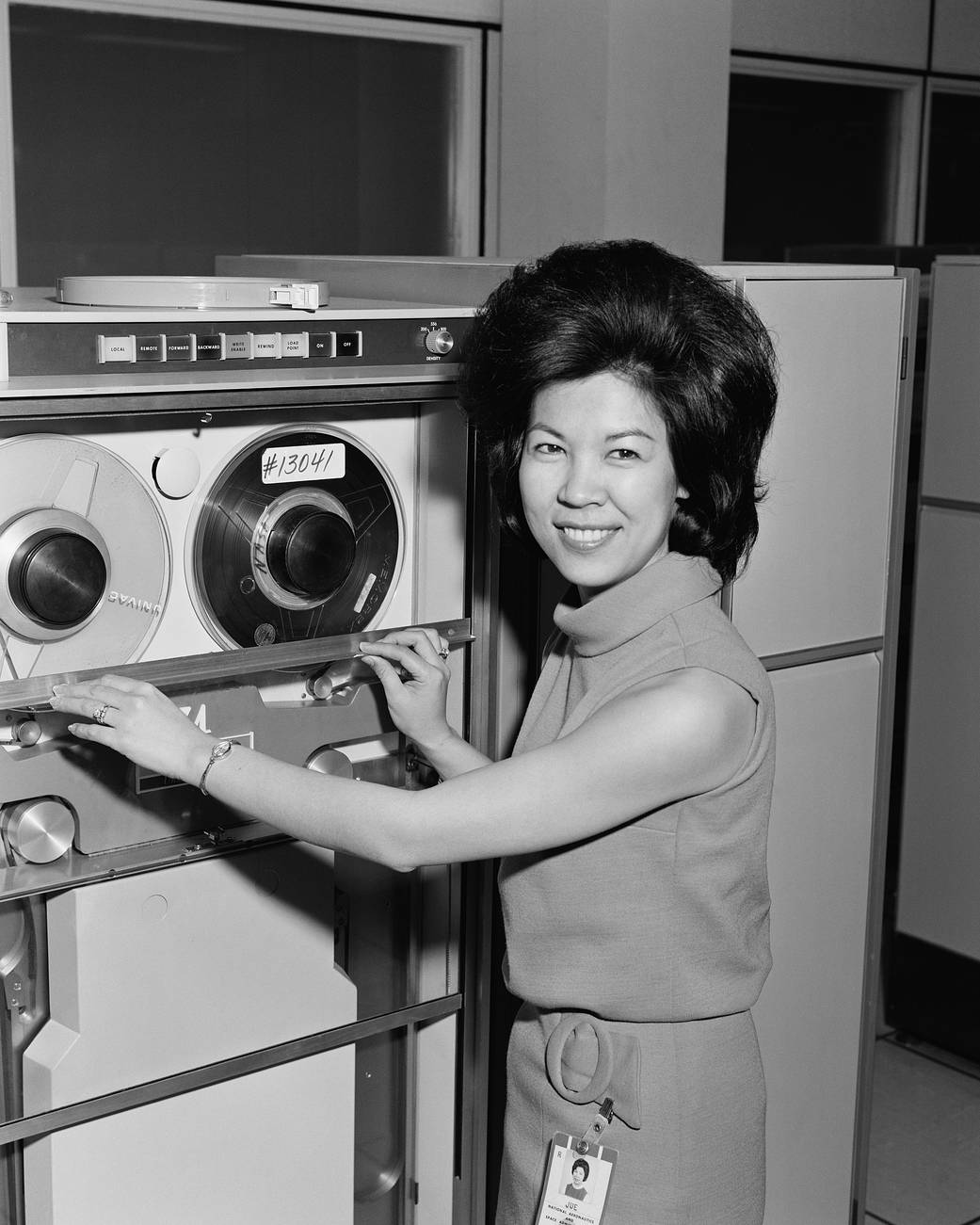 Portrait of Josephine Jue smiling as she poses with one of NASA Johnson Space Center's mainframe computers.