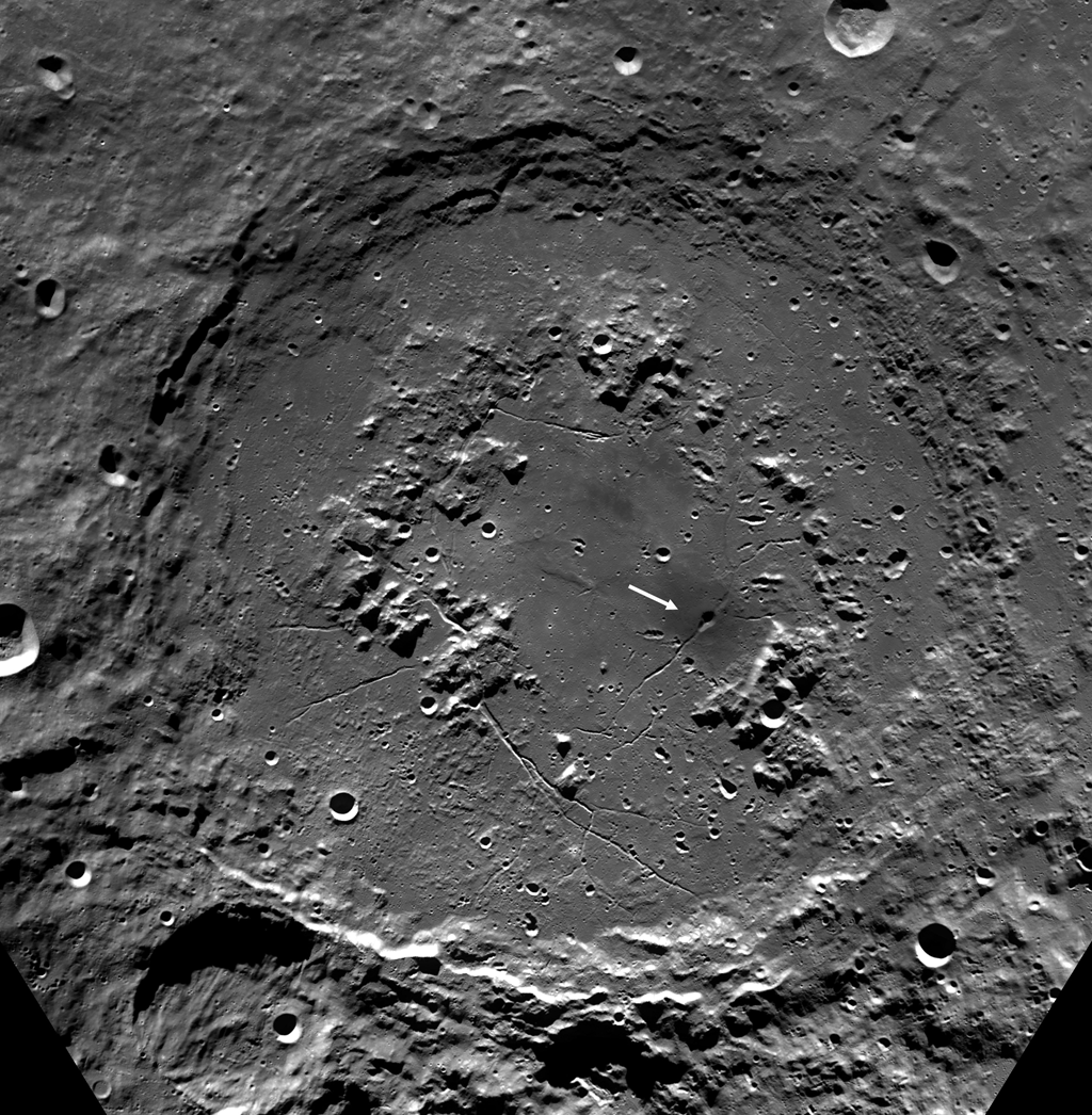 Mosaic of Clementine images of the Schrodinger Basin (312 km diameter). In addition to the prominent, dark, cone-shaped feature (white arrow), Schrodinger has an inner ring of mountains partially encircling the basin floor (a ‘peak ring complex’) and a network of radial and concentric fractures. The projection is polar stereographic, centered on the basin at - 75 ° S, 132 ° E.