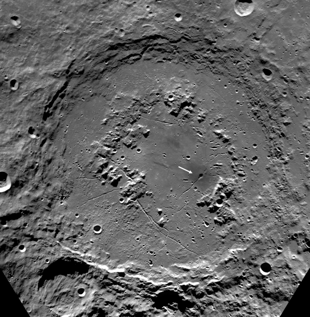 Mosaic of Clementine images of the Schrodinger Basin (312 km diameter). In addition to the prominent, dark, cone-shaped feature (white arrow), Schrodinger has an inner ring of mountains partially encircling the basin floor (a ‘peak ring complex’) and a network of radial and concentric fractures. The projection is polar stereographic, centered on the basin at - 75 ° S, 132 ° E.