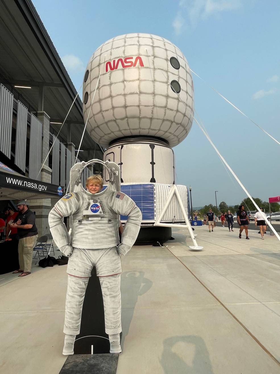 A youth attendee at Space Night, hosted by the Huntsville City Football Club, poses in an astronaut suit in front of an inflatable full-scale replica of a lunar surface habitat.