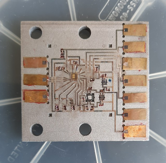 A white metal plate on a plastic surface with radian lines around it. On the plate are circuits and copper leads