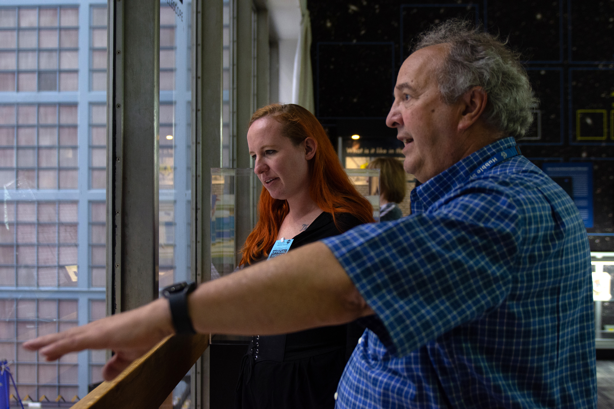 Two people looking through a window into a clean room with a full wall of square air filters visible within the clean room.