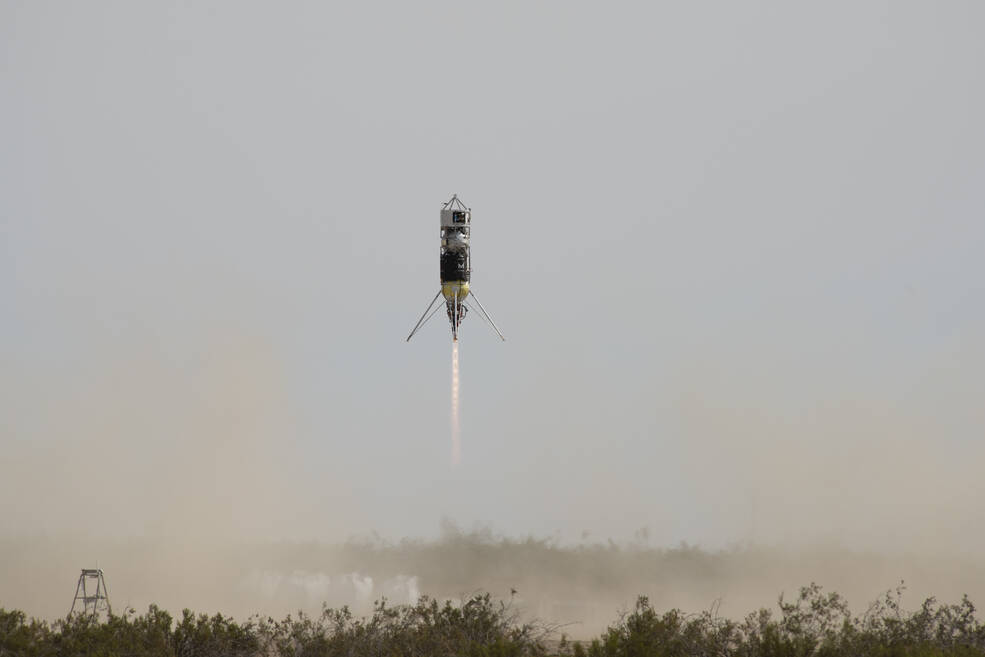 Rocket hovers above the ground. Legs that enable vertical landing emerge diagonally out the bottom.