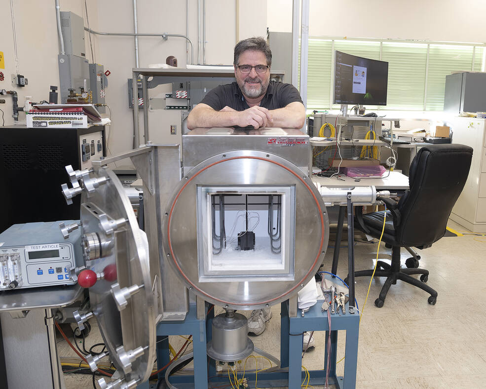 A man stands by what looks like a box with a door, like a microwave oven, to test a high-temperature sensor.