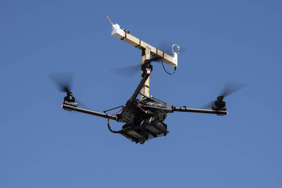 A quad rotor, remotely piloted drone hovers, while mounted sensors gather weather, temperature, pressure, relative humidity, and three-dimensional wind data.