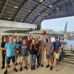 A group of people stand in front of a plane in a hanger.