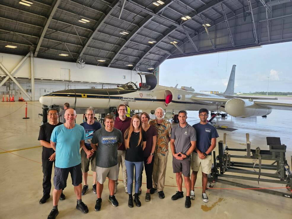 A group of people stand in front of a plane in a hanger.