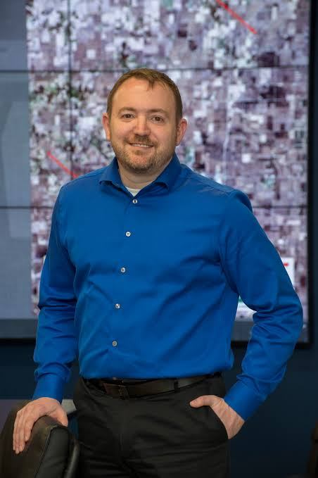 Image of Andrew Molthan standing in a blue shirt in front of artwork.
