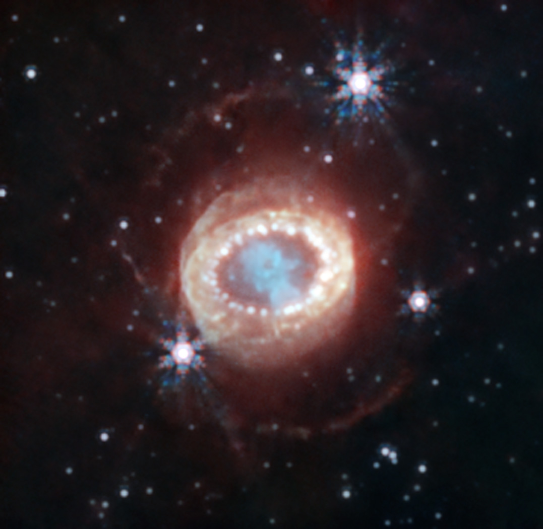 A pale red ring made up of small white circles surrounds a bright blue spot in the center. Three bright spots are on the outside of the ring, all against a black background speckled with stars.