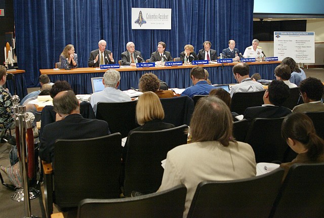 Representatives of CAIB sit behind a table in front of a group of reports during a press briefing.