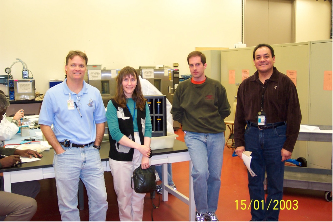 Image of four people standing with KSC technical staff working on assembly of Columbia nematode hardware (photo credit D. Reed)