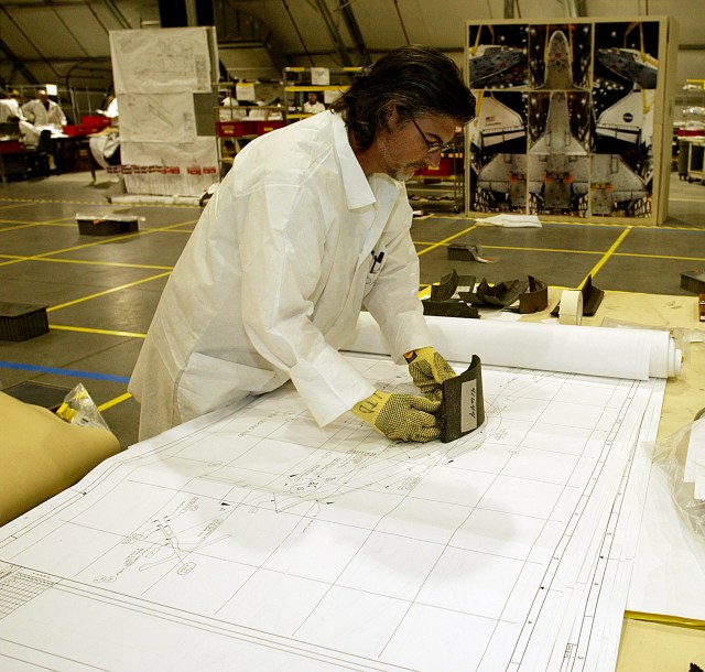 A reconstruction team member holds a piece of debris to a 1:1 engineering drawing to help identify it.