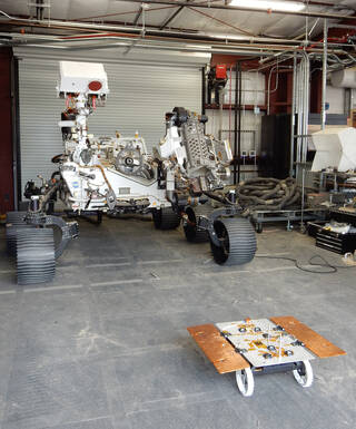 A CADRE test rover appears to catch the attention of the much larger engineering model of NASAs Perseverance rover, called OPTIMISM, at JPLs Mars Yard.