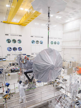 Engineers and technicians use a crane to lift a 10-foot (3-meter) high-gain antenna as they prepare to install it on NASAs Europa Clipper spacecraft.