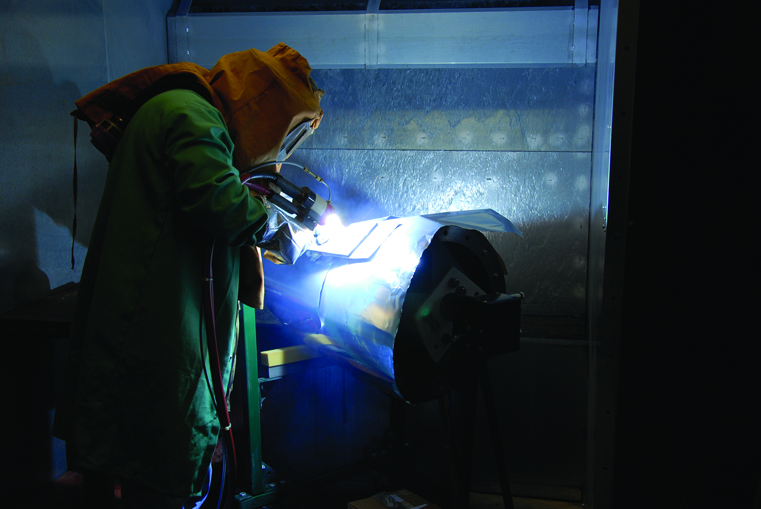 A man in gloves, a helmet, and a jacket, uses a torch to attach a high-temperature sensor.