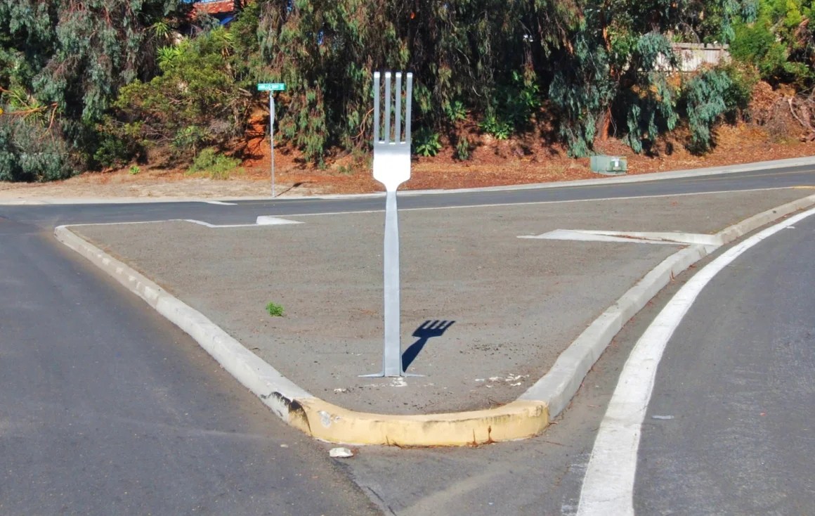 "A fork in the road"(metaphor) showing a silver fork on an island on the road.