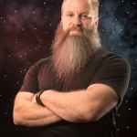 Portrait of Graham Lau from Blue Marble Space, with chest length brown and white goatee beard, wearing a brown shirt with a black bracelet on his wrist.