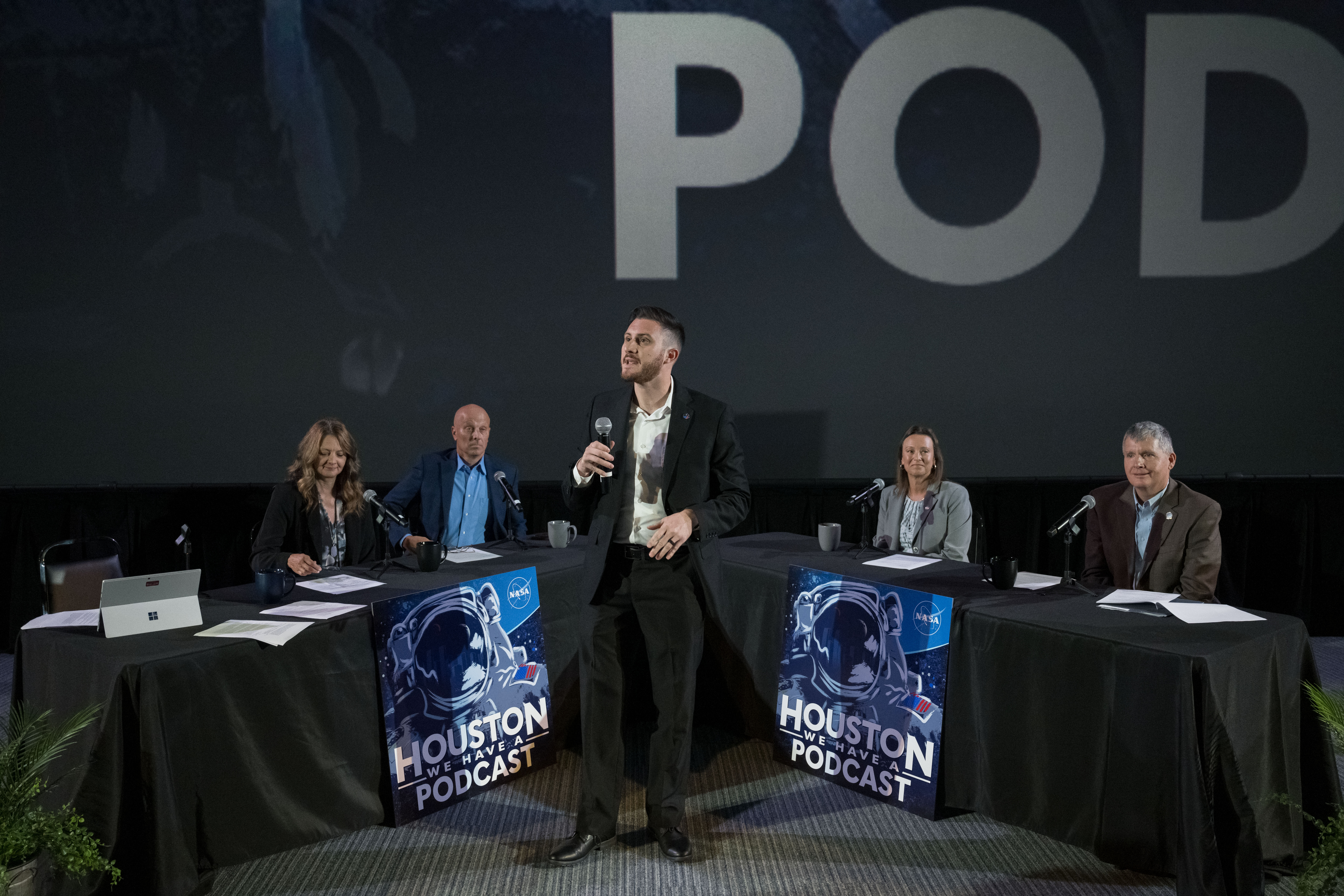 A wide shot of a stage. In the center is the host, Gary Jordan. Behind (from left) is Angela Hart, Steve Koerner, Dina Contella, and Steve Stich all sitting at tables as they discuss the future of a presence in low Earth orbit.