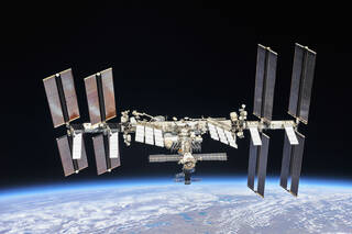 The International Space Station orbiting above Earth. Four large pairs of solar panels are seen on either side of the station.