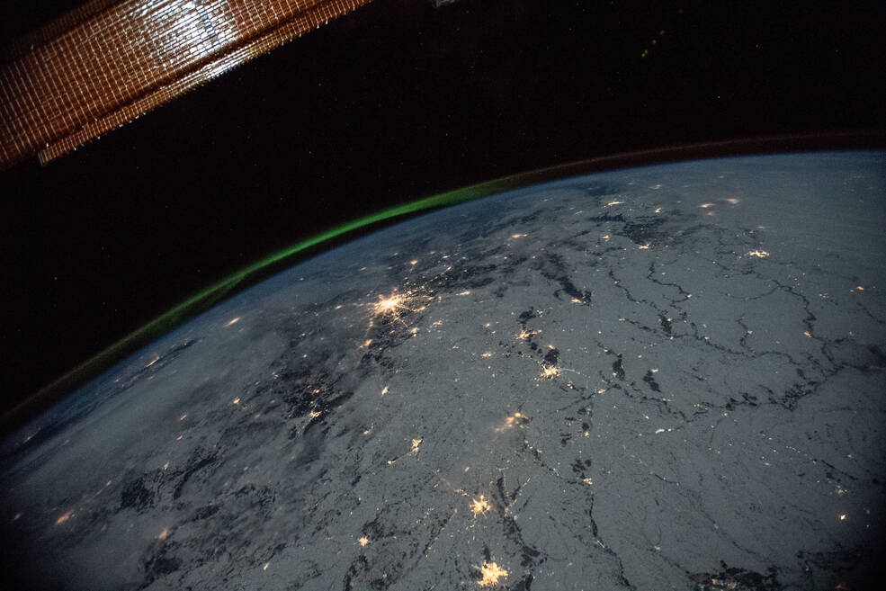 Earth at night from space, with aurora above and the space stations solar array in the foreground.