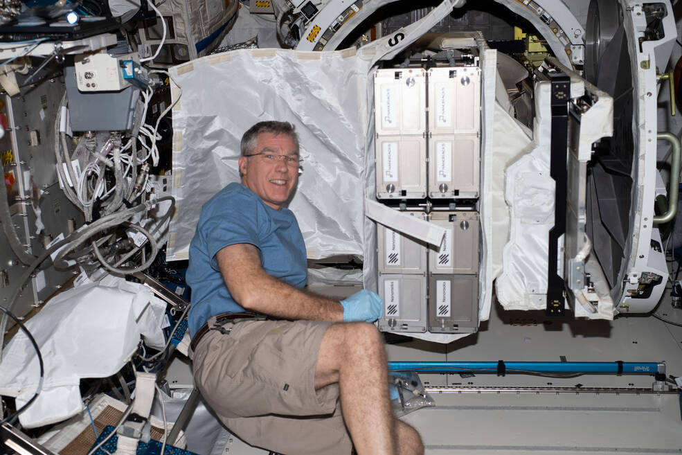NASA astronaut Stephen Bowen poses on the station with CubeSats to be deployed from the space station for the 26th NanoRacks CubeSat Deployer (NRCSD-26) mission.