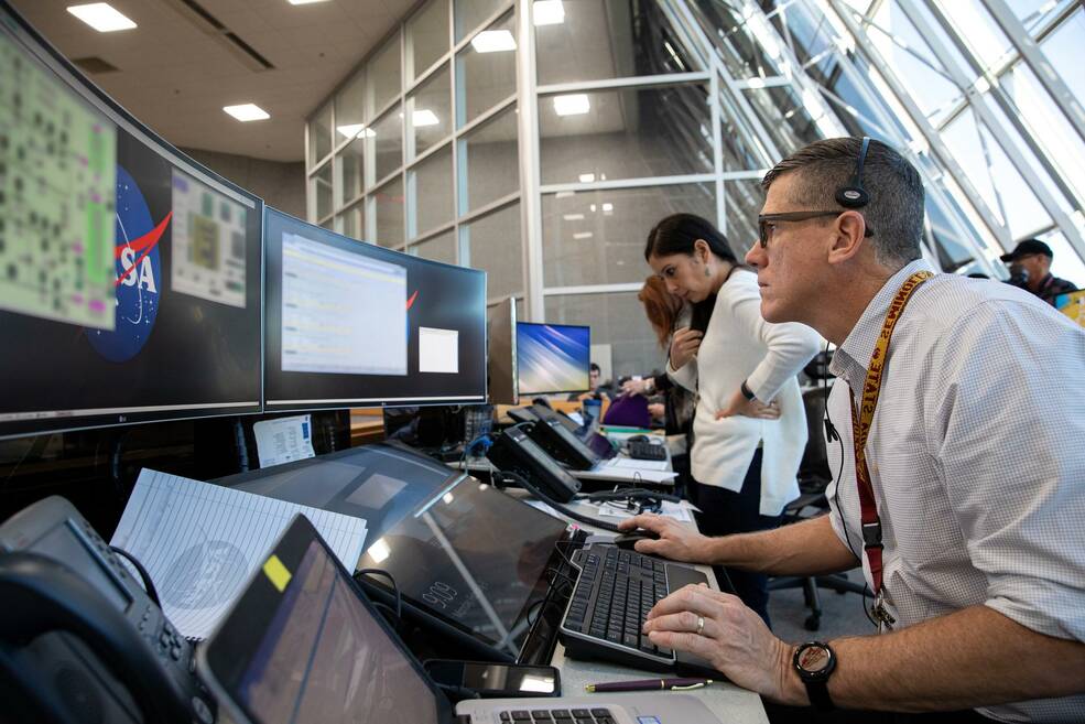 A person peers at a computer screen in a busy launch control center.