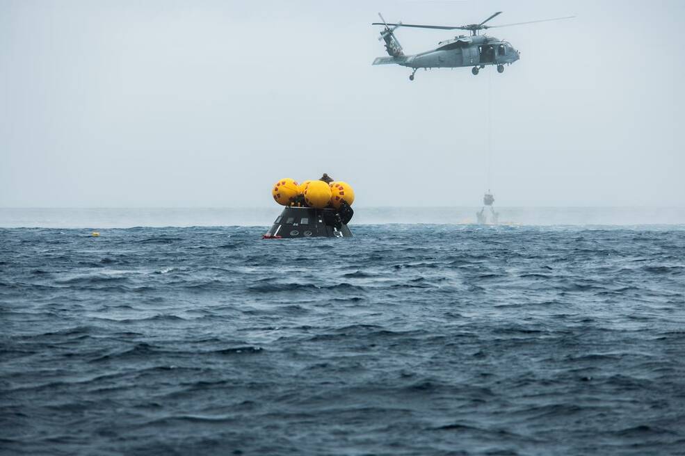 In this photo Naval helicopter pilots lift a pilot in a basket from an inflatable front porch that allows astronauts to be recovered out of the Orion spacecraft.