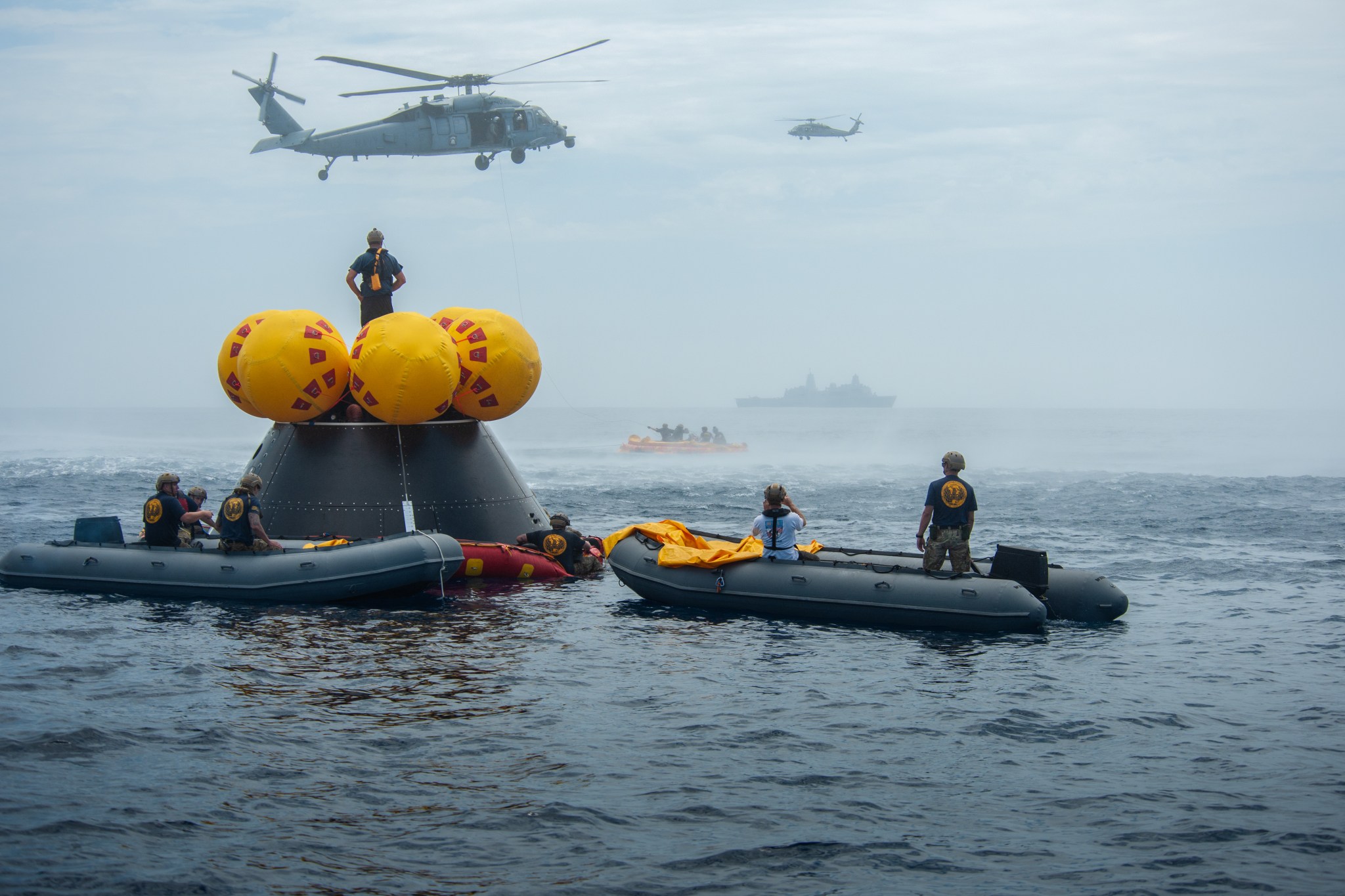 Naval helicopter pilots from Helicopter Sea Combat Squadron (HSC) 23 “Wildcards” fly over the Orion Crew Module Test Article (CMTA) with American flags after completing flight operations during an Artemis II mission simulation during NASA’s Underway Recovery Test 10 (URT-10) off the coast of San Diego.