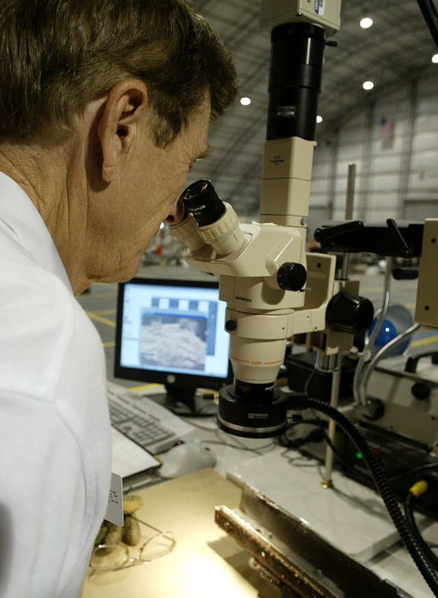 A man peers through a microscope at a piece of debris from the Columbia accident