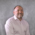 Image of Andrew Molthan standing in a pink shirt in front of a plain studio background.